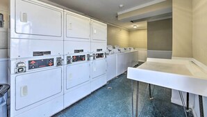A laundry room with multiple washing machines and dryers, a white counter, and a blue tiled floor. - Oceanfront Panama City Beach Condo w/ Pool Access (Panama City Beach)