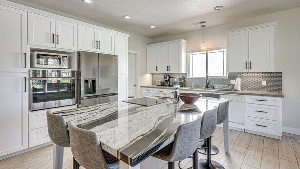 A modern kitchen with white cabinetry, a central island with bar stools, stainless steel appliances, and a view of the outdoors. - Spacious Mesquite Getaway - 1/2 Mi to Golf Course (Mesquite)