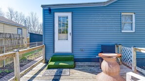 Ein blaues Haus mit einer weißen Tür, einer kleinen Veranda mit hölzernem Geländer und einem runden Tisch mit Flechtgeflecht.