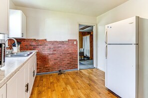 Een keuken met een bakstenen muur, houten vloer, witte kastjes en een witte koelkast.