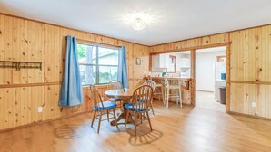 A wooden-paneled room with a dining table and chairs, a window with curtains, and a kitchen area visible through an open doorway. - Lakefront Keystone Heights Cottage w/ Private Dock (Keystone Heights)