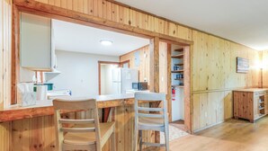 A wooden interior with a kitchen area featuring a refrigerator, microwave, and wooden cabinets. There are two wooden chairs at a table. - Lakefront Keystone Heights Cottage w/ Private Dock (Keystone Heights)