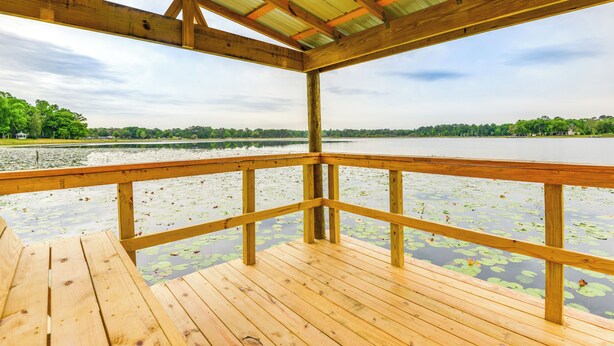 A wooden deck with a metal roof overlooking a lake with lily pads. - Lakefront Keystone Heights Cottage w/ Private Dock (Keystone Heights)