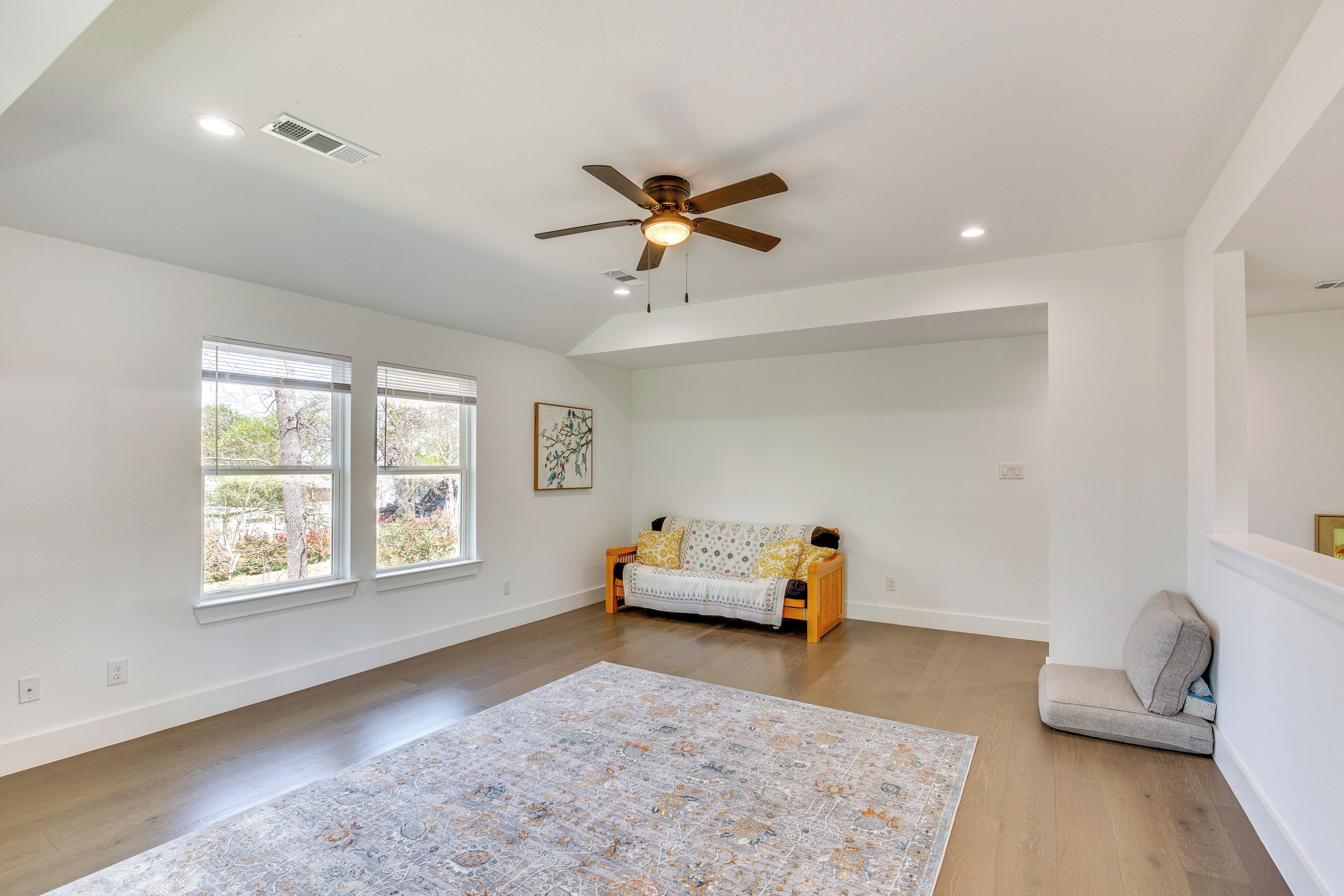 A spacious room with a ceiling fan, large windows, a sofa, and a rug.