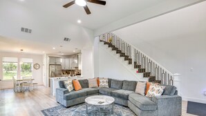 A spacious living room with a gray sectional sofa, a round coffee table, and a patterned rug. A staircase with a black railing leads to an upper level. - Fire Pit + Grill: Lakeside Gun Barrel City Home! (Mabank)