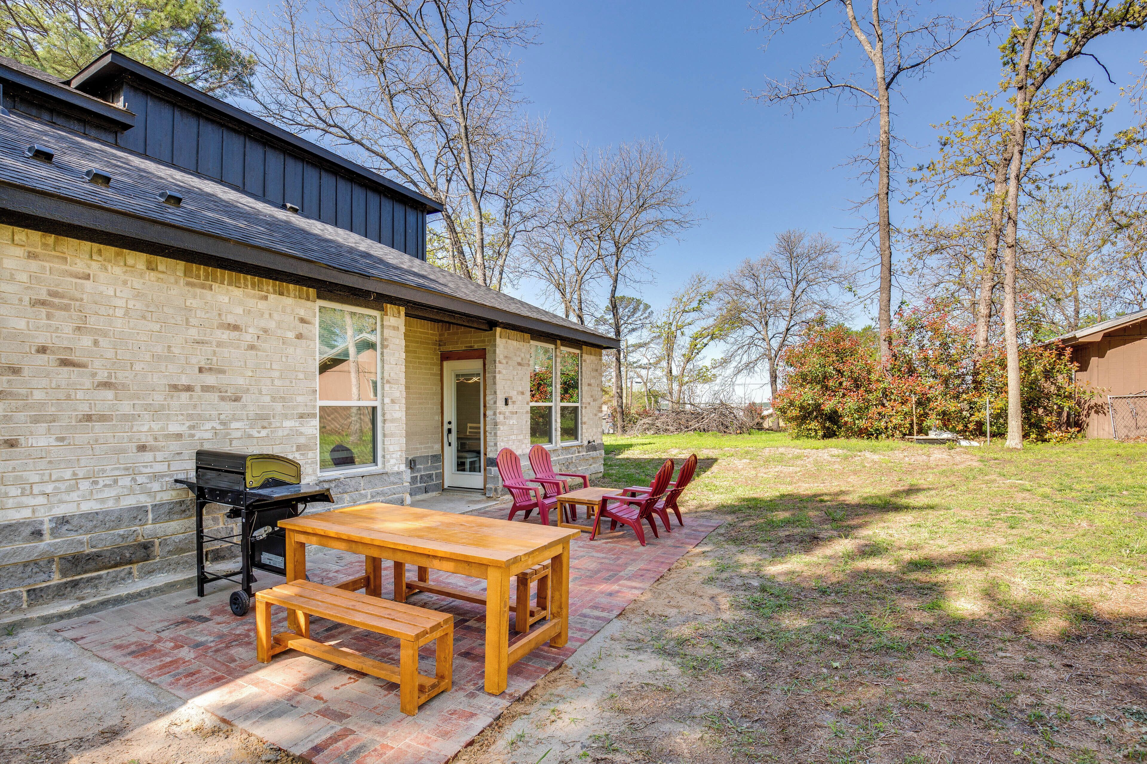 A patio with a wooden table and chairs, a grill, and a brick wall.