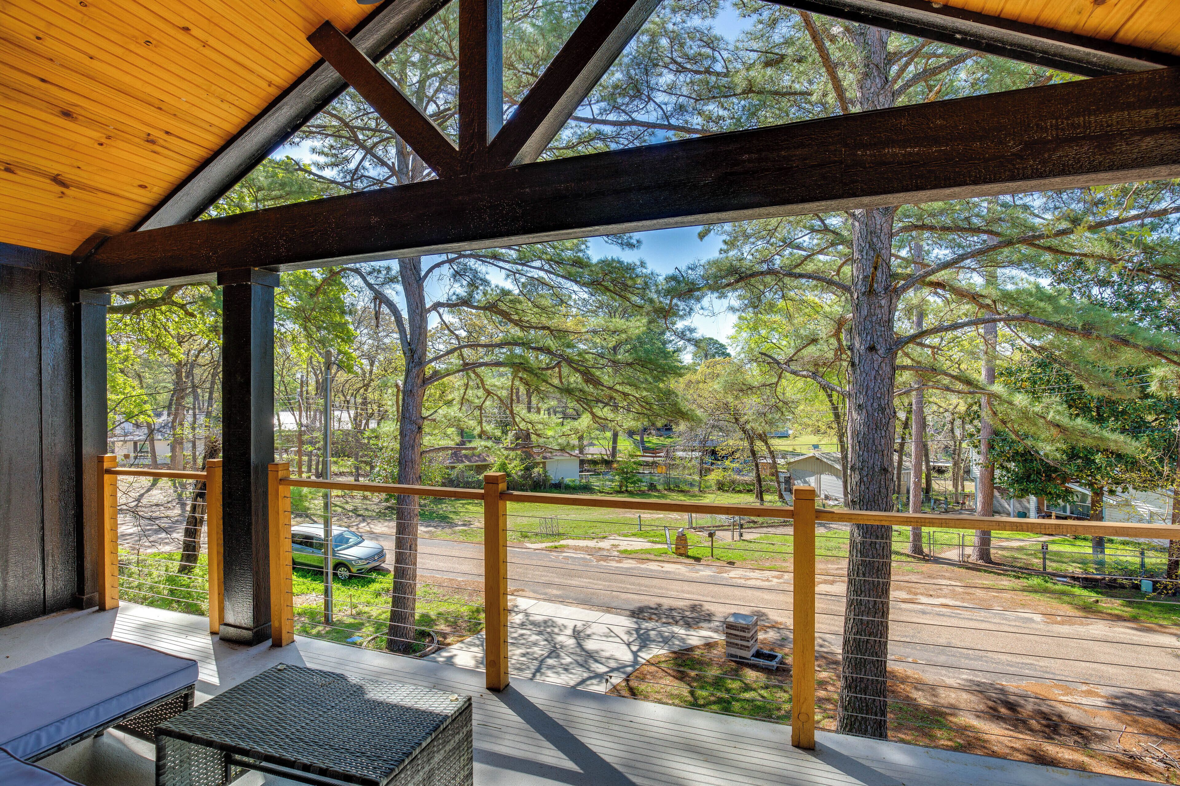 A covered outdoor area with a wooden deck, a bench, and a view of a residential street with houses and trees.