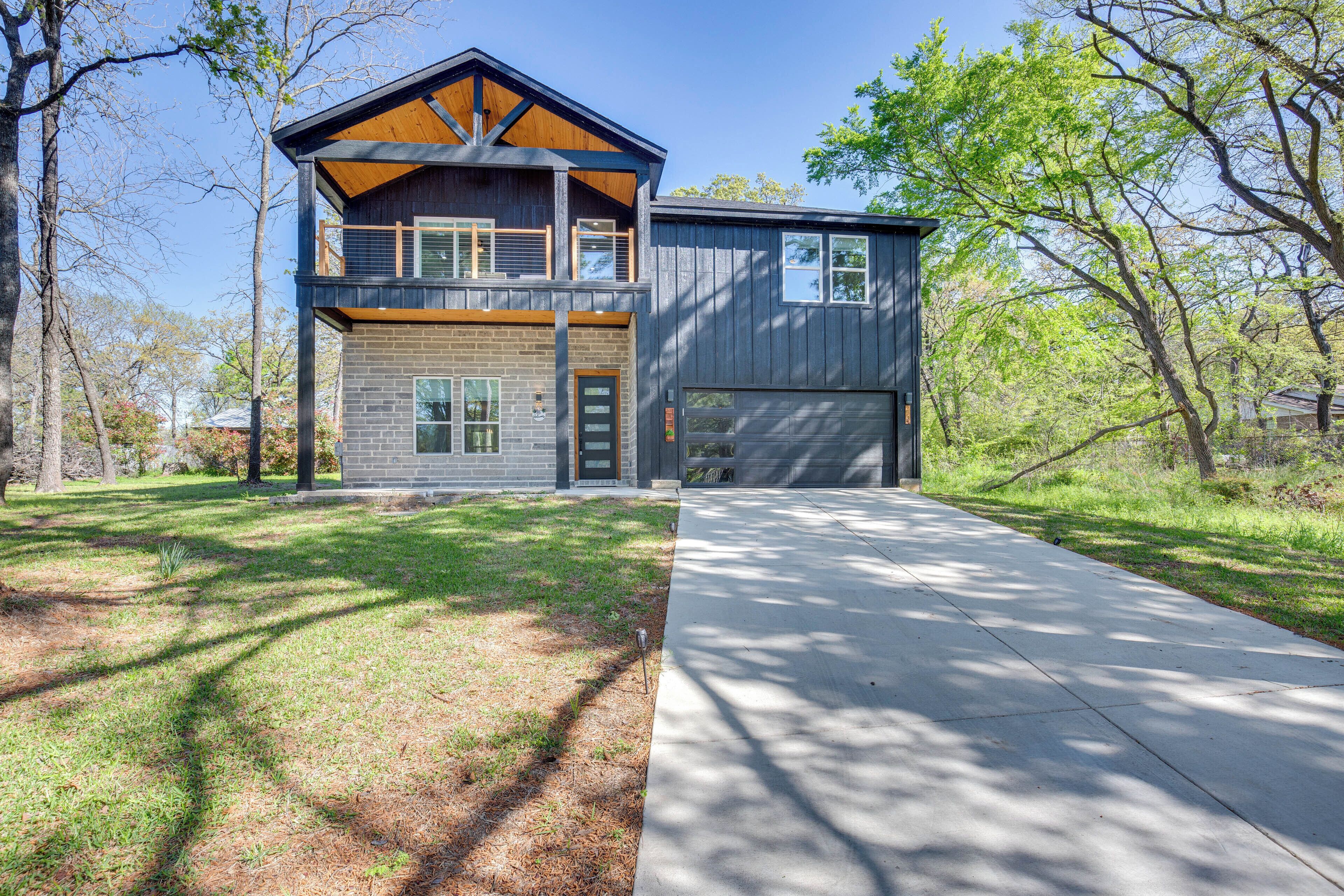 Une maison à deux étages avec un garage, une pelouse devant et des arbres en arrière-plan.