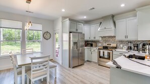 A modern kitchen with white cabinetry, a stainless steel refrigerator, a microwave, and a large island with a sink. - Fire Pit + Grill: Lakeside Gun Barrel City Home! (Mabank)