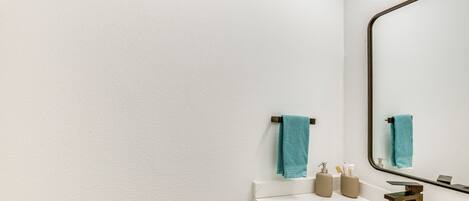 A modern bathroom with a white marble sink, a large mirror, and two towels hanging on towel racks.
