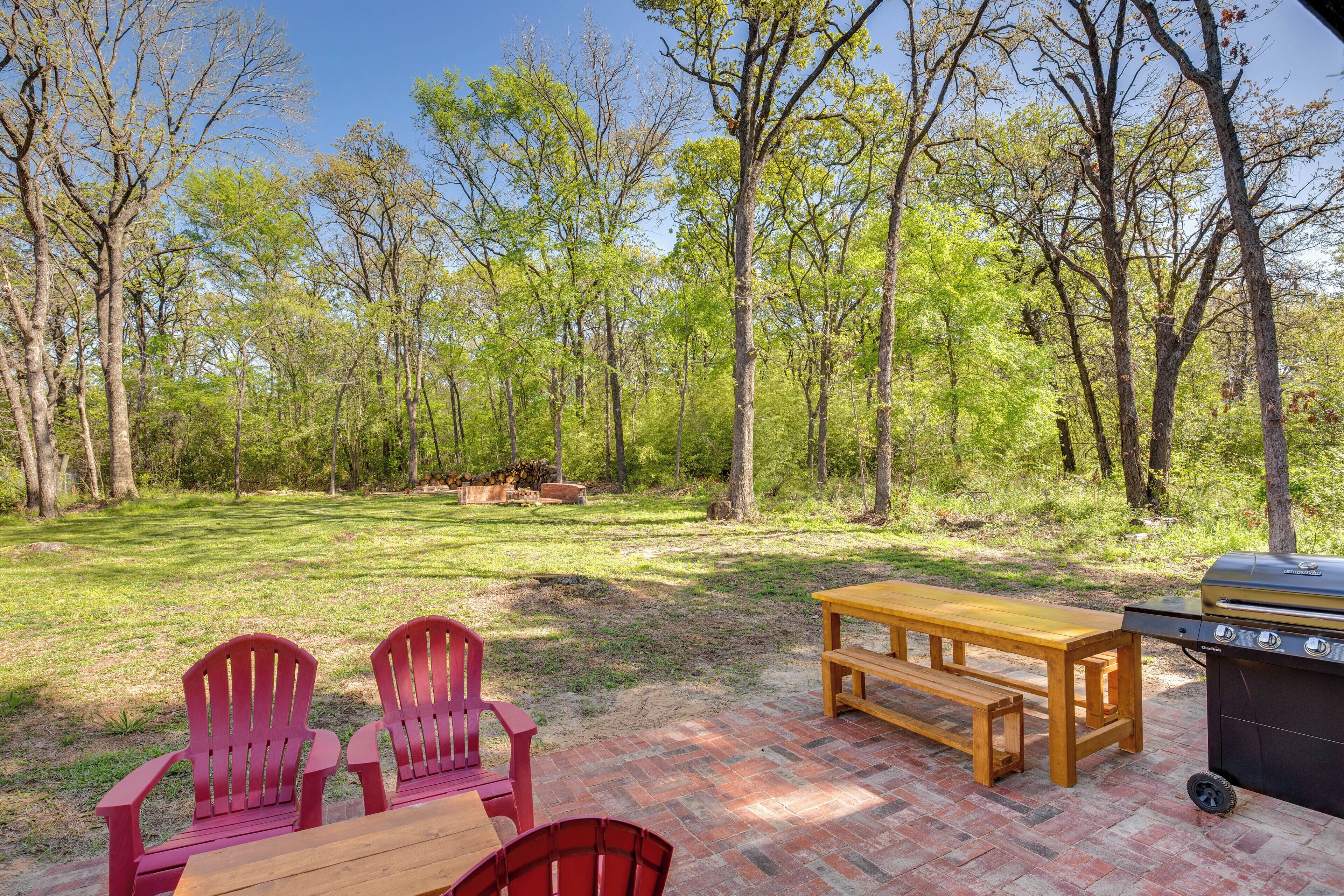 A patio area with a grill, red Adirondack chairs, and a wooden table.