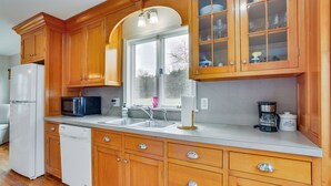 Una cocina con armarios de madera, un refrigerador, un microondas, un lavamanos y un ventanal.