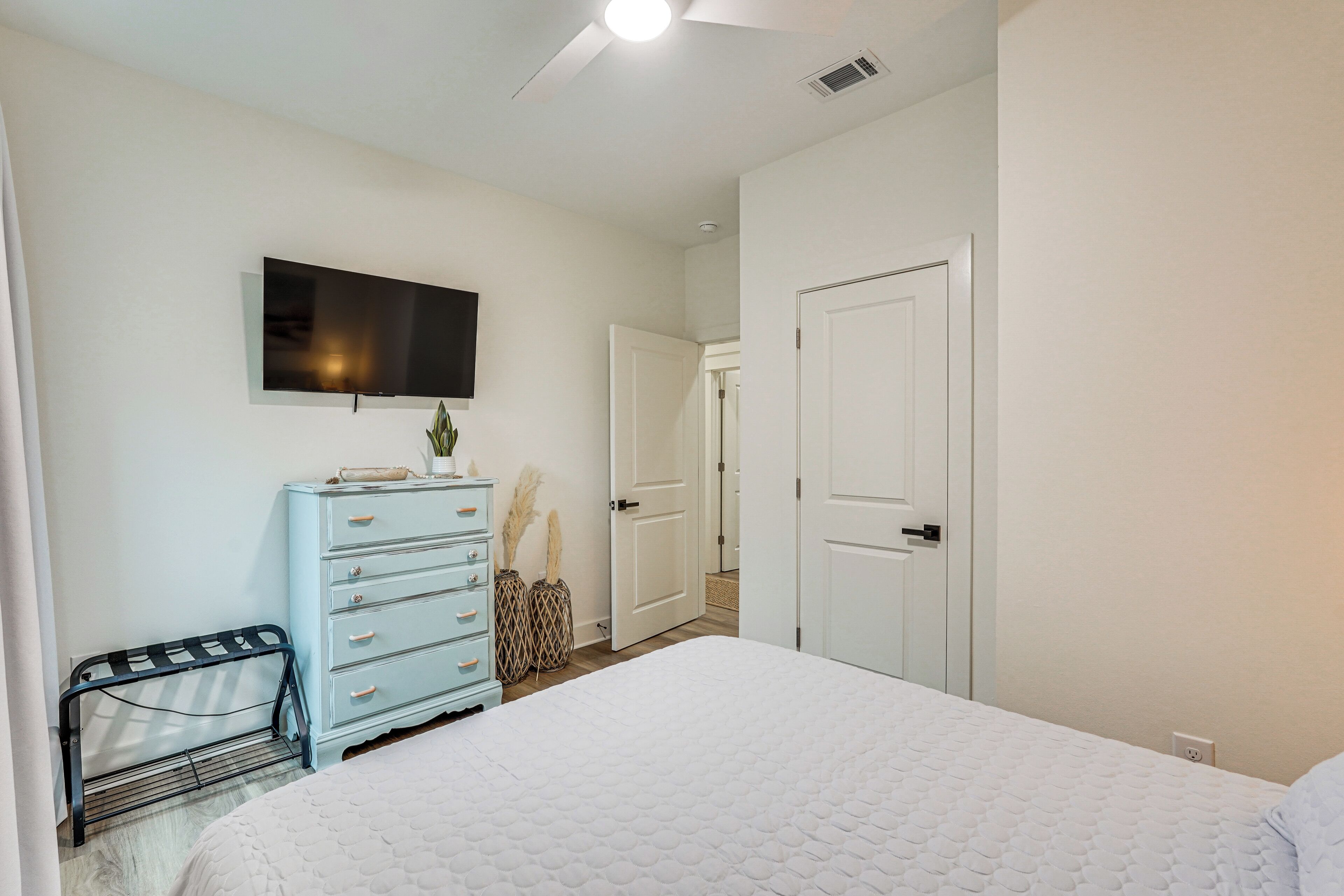 A bedroom with a bed, dresser, TV, and a door leading to another room.