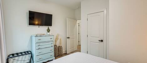 A bedroom with a bed, dresser, TV, and a door leading to another room.