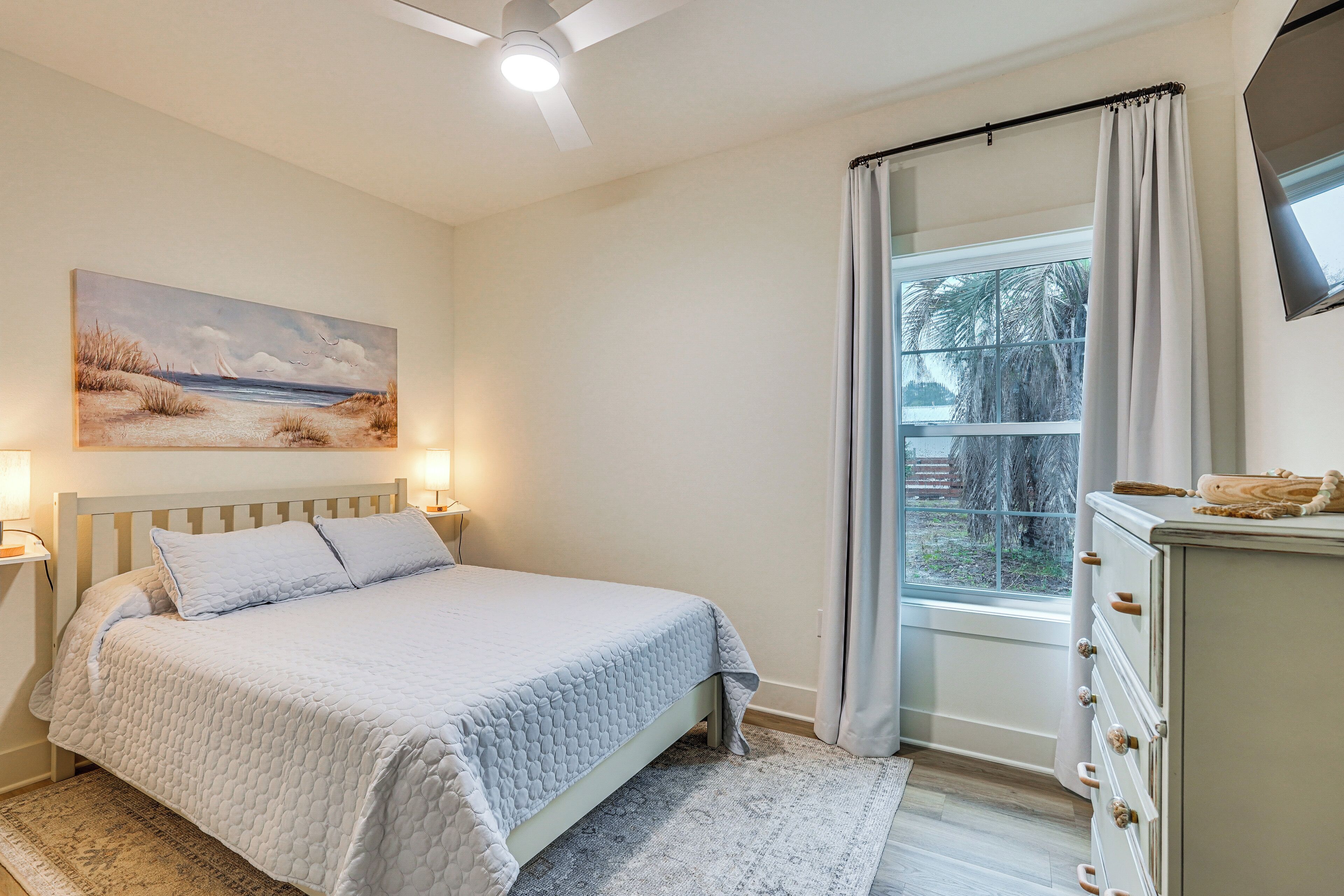 A bedroom with a bed, a painting, a window with curtains, and a dresser.