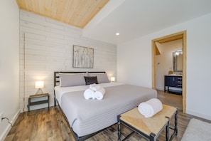 A bedroom with a large bed, bedside lamps, a wooden floor, and a painting on the wall. - Pisgah Forest Retreat w/ Fire Pit, Grill & Views! (Pisgah Forest)