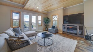 A living room with a wooden ceiling, a large flat-screen TV, a sofa, a coffee table, and a patterned rug.