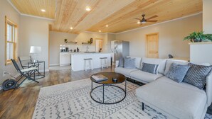 A spacious living area with a wooden ceiling, a sofa, a coffee table, and a kitchen in the background.