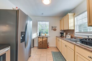 Una cocina con refrigerador de acero inoxidable, armarios de madera, una ventana con persianas y un letrero que indica barra de café.