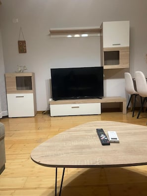 A modern living room with a flat-screen TV, wooden furniture, and a coffee table with remote controls. - Kalpazo Home Skanderbeg Square (Tirana)
