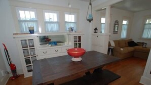 Une cuisine avec une table en bois, un saladier rouge et une fenêtre avec des rideaux.