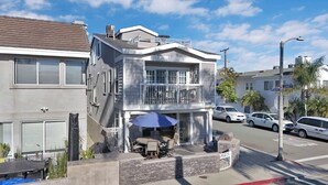 A two-story residential building with a balcony, a covered outdoor seating area, and a garage. - 223 34th St A | Beautiful beach house, 2 blocks to the sand (Newport Beach)