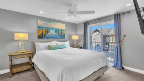 A bedroom with a large bed, two bedside tables with lamps, a ceiling fan, a painting of a bridge, and a view through a glass door. - 223 34th St A | Beautiful beach house, 2 blocks to the sand (Newport Beach)