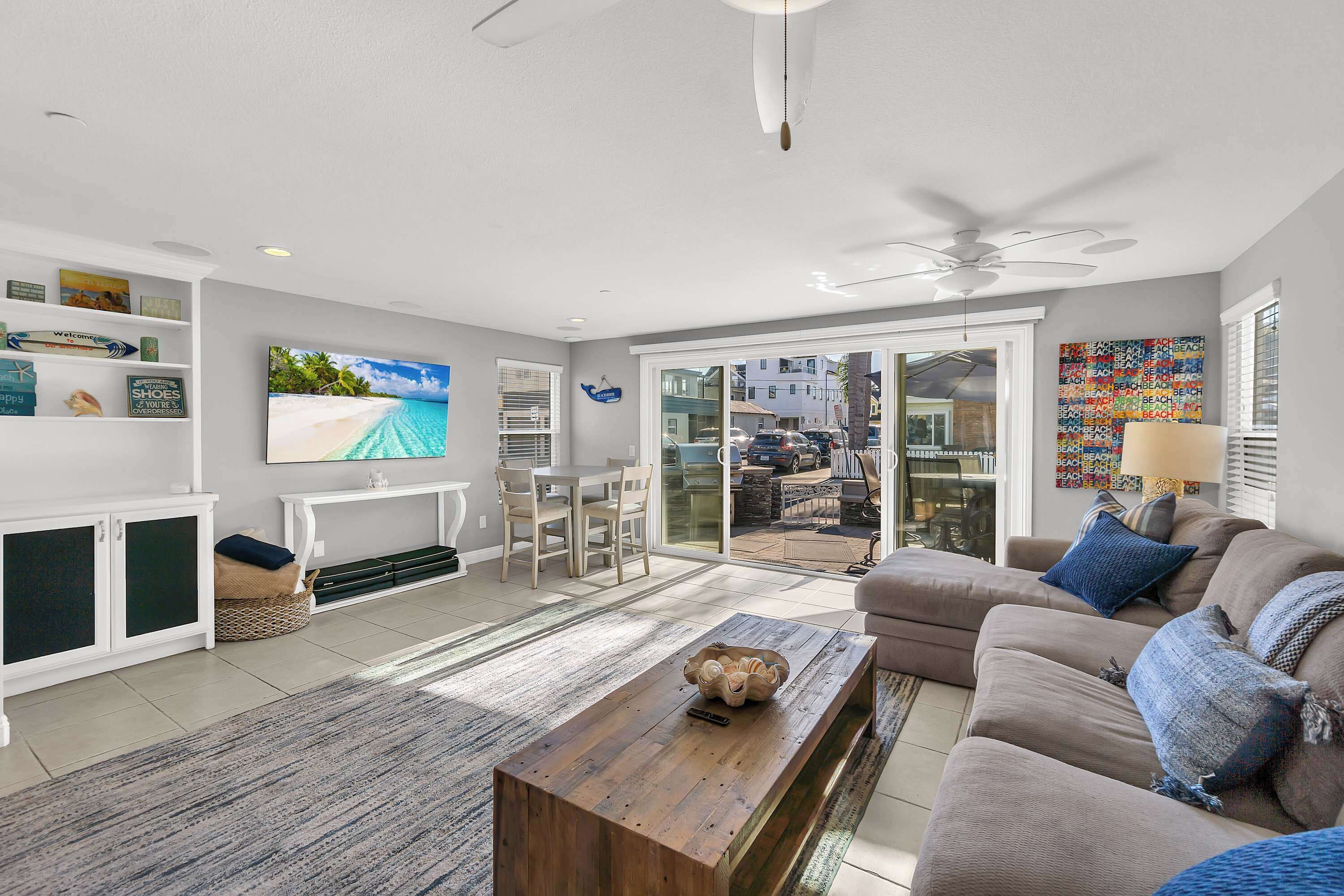A spacious living room with a flat-screen TV, a wooden coffee table, a beige sofa, and a large sliding glass door leading to an outdoor area.