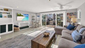 A spacious living room with a flat-screen TV, a wooden coffee table, a beige sofa, and a large sliding glass door leading to an outdoor area. - 223 34th St A | Beautiful beach house, 2 blocks to the sand (Newport Beach)