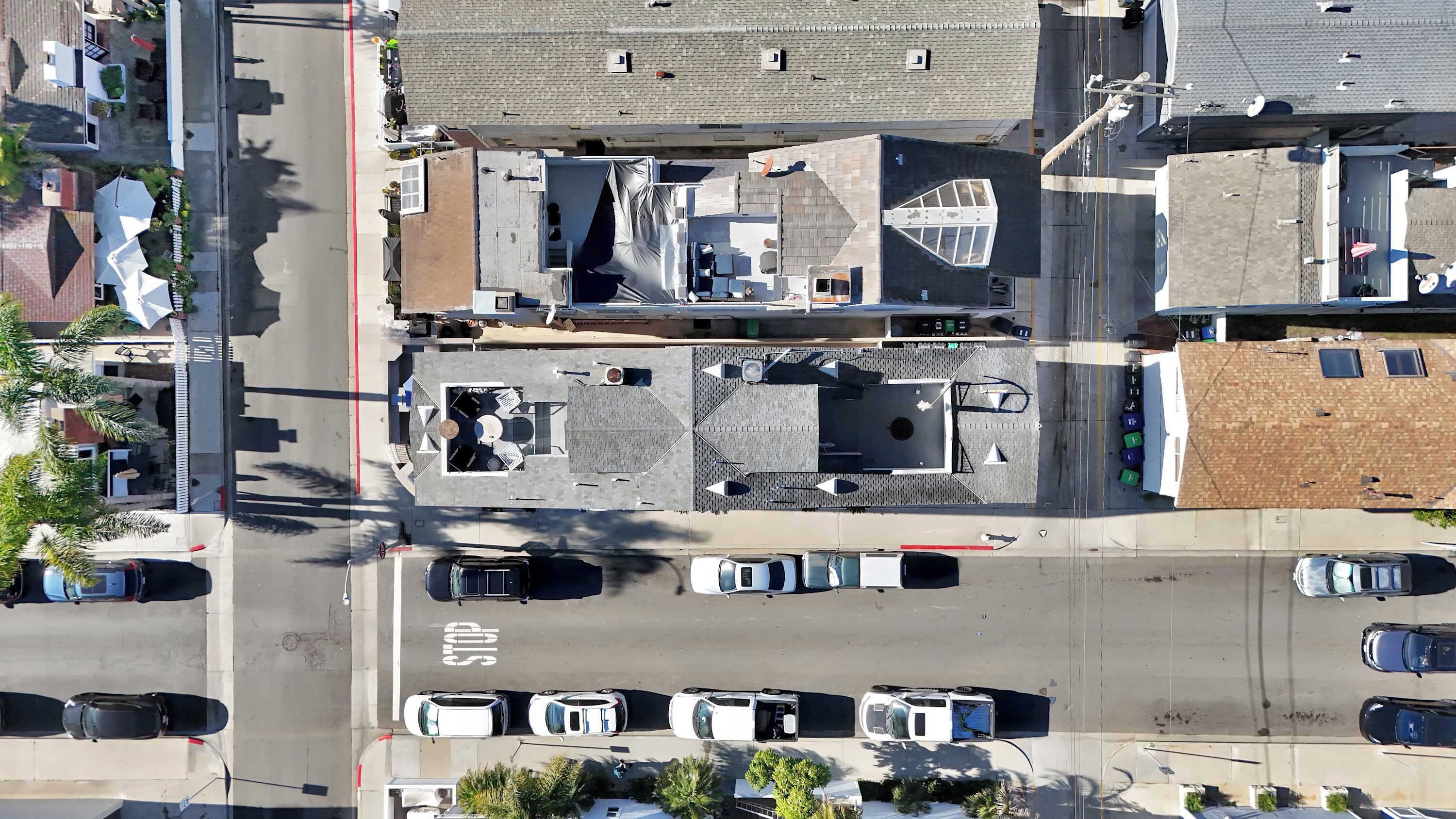 An aerial view of a parking lot with multiple cars, a stop sign, and buildings with various roof designs.