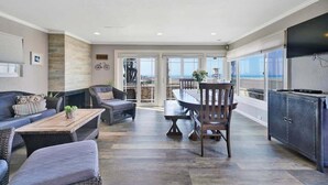 A spacious living area with a dining table, sofas, and a large TV.