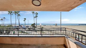A balcony with a view of a beach, palm trees, and a lifeguard tower.