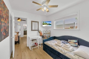 A room with a bed, a desk, a chair, a ceiling fan, a window with a view, and a painting on the wall. - Lower Unit, Close to Restaurants, and Shopping (Newport Beach)