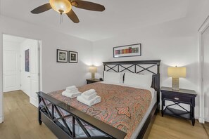 A hotel room with a bed, a ceiling fan, two bedside tables with lamps, and a door leading to another room. - Lower Unit, Close to Restaurants, and Shopping (Newport Beach)