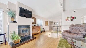 Uma sala de estar ampla com lareira, televisão na parede e um espaço de estar confortável com sofá e mesa de centro de vidro.