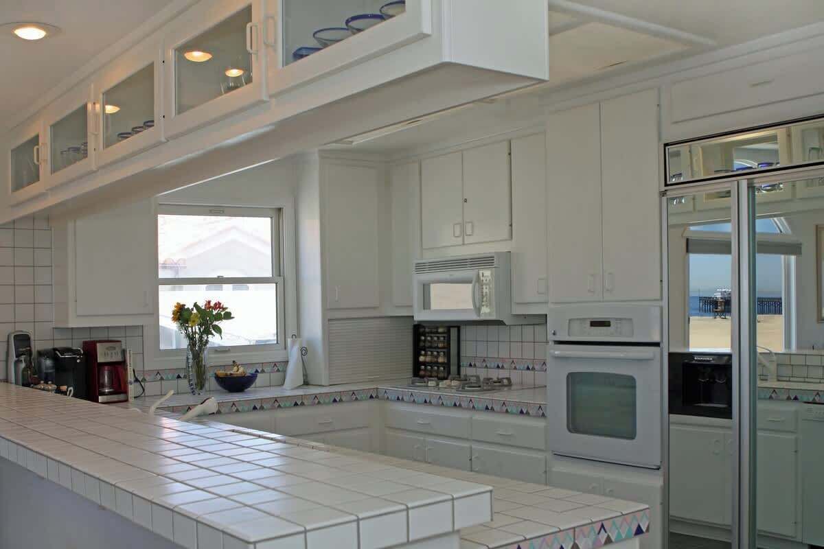 A modern kitchen with white cabinetry, a central island, and a view of the beach.