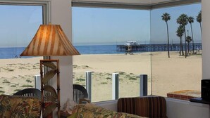 Habitación con grandes ventanales que dan a una playa, con una lámpara, una silla y vistas al océano y un muelle.
