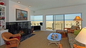 Una sala de estar con chimenea, televisor y un ventanal con vista a la playa.