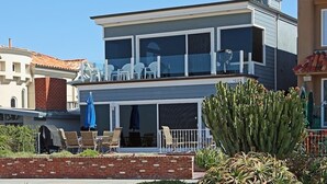 Una casa moderna de dos pisos con balcón, mobiliario exterior y un gran cactus al frente.