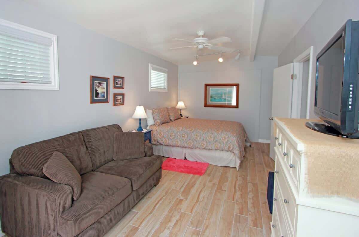 A bedroom with a bed, a brown sofa, a ceiling fan, a television, and a dresser.