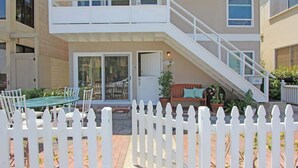 A two-story residential building with a white exterior, a balcony, and a staircase leading to the upper floor. - 1009 W Bay | Quaint Cottage Steps to Sand (Newport Beach)