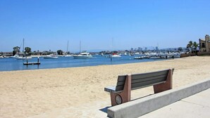 A beach with a bench and a marina filled with boats. - 1009 W Bay | Quaint Cottage Steps to Sand (Newport Beach)