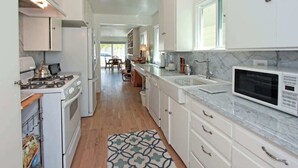 A compact kitchen with white cabinets, a microwave, a stove, and a sink. - 1009 W Bay | Quaint Cottage Steps to Sand (Newport Beach)