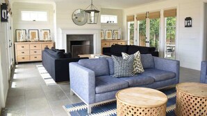 A spacious living room with a grey sofa, a fireplace, and a large window. - 1028 W Oceanfront | Beautiful 5bdr Beachfront on Scenic Bike Path (Newport Beach)