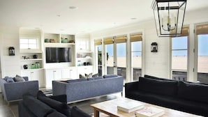 A modern living room with a large TV, grey sofas, and a coffee table. - 1028 W Oceanfront | Beautiful 5bdr Beachfront on Scenic Bike Path (Newport Beach)