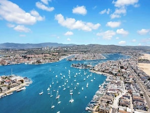 An aerial view of a coastal city with a marina filled with boats, a densely packed urban area, and a clear blue sky. - Newport Beach Bayside Home, Wrap-Around Patio and Bay Views (Newport Beach)