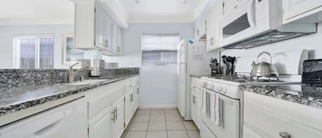 Una cocina moderna con armarios blancos, encimeras de granito, horno empotrado y microondas.