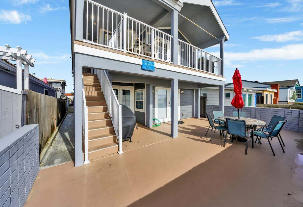 A two-story building with a covered patio area featuring a table and chairs, a red umbrella, and a staircase leading to the upper level.