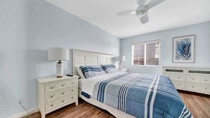 A bedroom with a bed, nightstands, a ceiling fan, a window with blinds, and a wall-mounted artwork. - 1404 W Oceanfront A | Value Beachfront w/Large Patio On The Bike Path (Newport Beach)