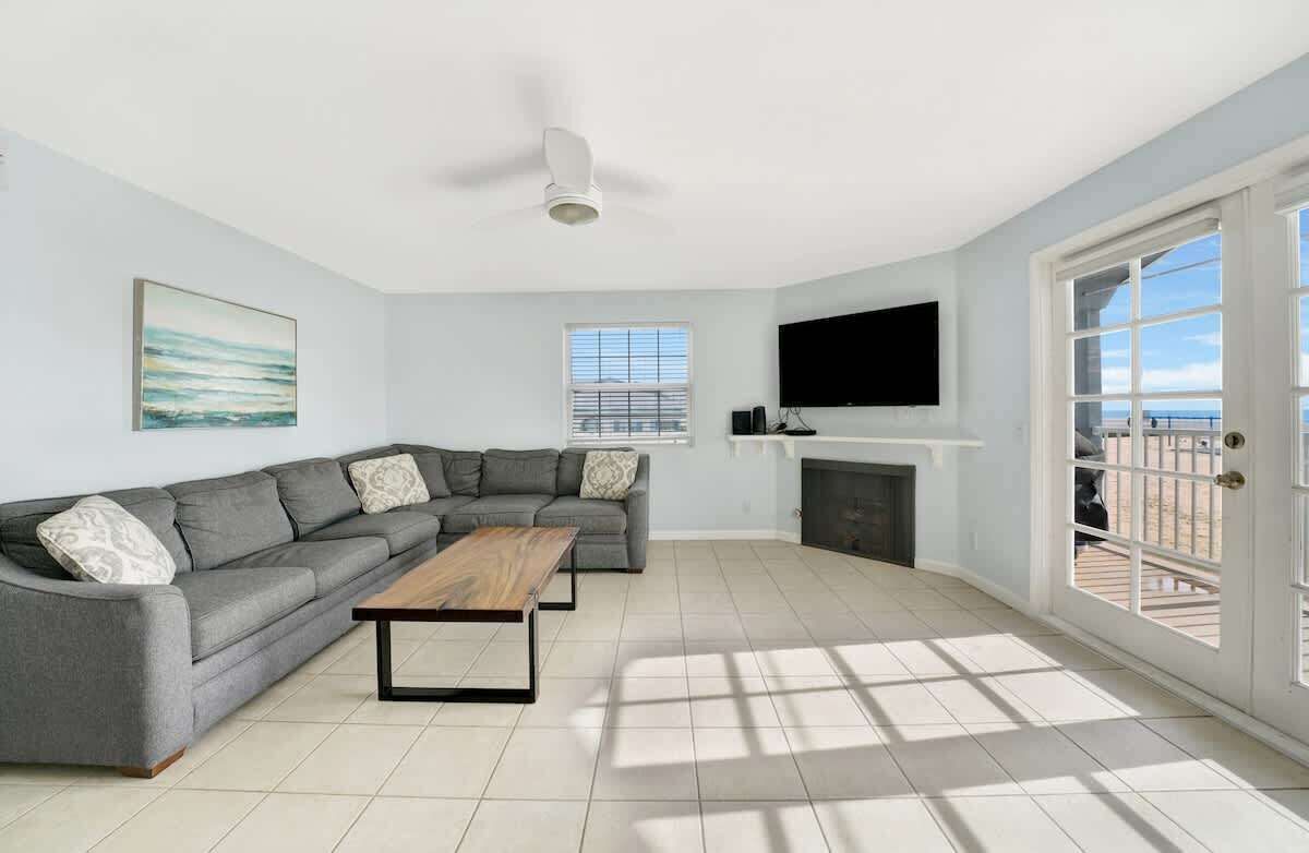 A living room with a grey sectional sofa, a wooden coffee table, a ceiling fan, a flat-screen TV, and a fireplace.